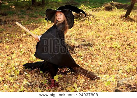 Photo d'une petite fille en costume d'halloween posant avec balai et citrouille en plein air.