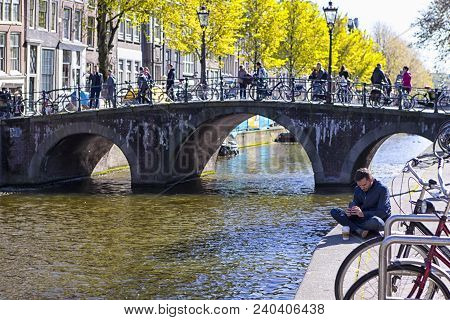 Amsterdam, Netherlands - May 8, 2017:  Man Reading And Drinking Coffee In Front Of One Of The Canals