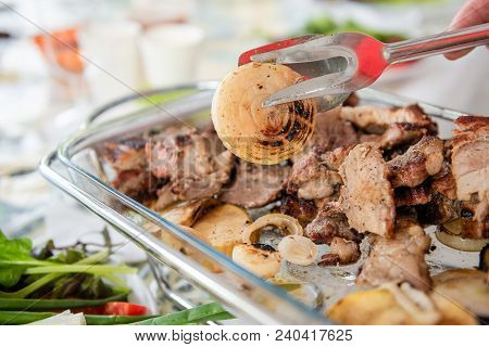 Table With Barbeque Grilled Meat, Vegetables And Greens.tongs Catch Piece Of Grilled Onion.