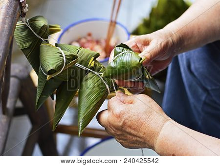 Two Hands Tighten Strings Over Leaf To Make Zongzi, The Traditional Chinese Rice Dumplings For Drago
