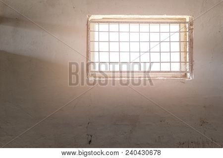Old White Wall With Window Covered By Iron Grate. Sun Shining  Through Grill. Mental Prison . Enligh