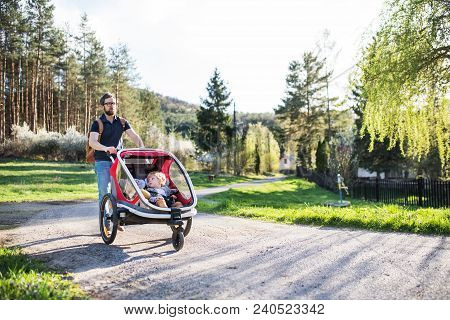 A Father With Two Toddler Children Sitting In Jogging Stroller On A Walk Outside In Spring Nature.