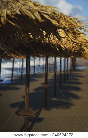 Vacation, Travel, Beach And Beach Umbrellas From The Straw During The Tide. Sea Waves And Empty Sand