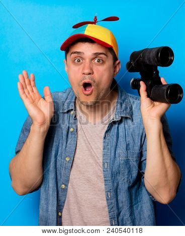 Young Nerd Man With Noob Hat Using A Binoculars On Blue Background
