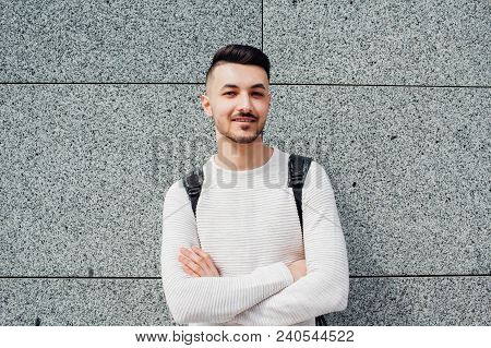 Arabian Student With Backpack Standing By Stone Wall Outside. Young Smiling Man With Crossed Hands W