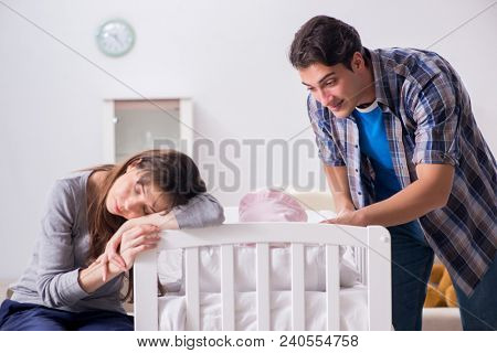 Young parents with their newborn baby near bed cot