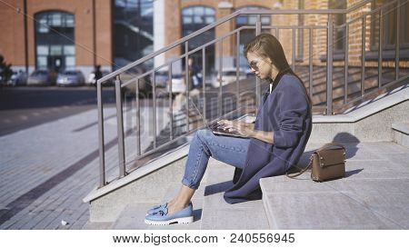 A Young Girl In Jeans In Sunglasses Is Working With A Laptop Outisde Drinking Coffee