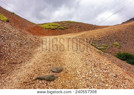 A Gravel Steep Red Road In Lonsoraefi, Iceland In Cloudy Weather