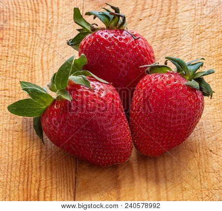 Three Strawberries With Leaves On Wooden Chopping Board