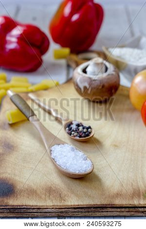Salt And Pepper In Wooden Spoons Surrounded By Vegetales.