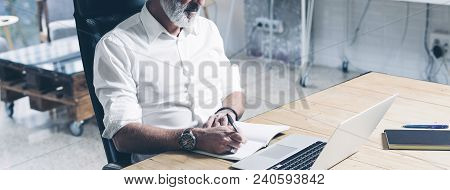 Attractive And Confidental Adult Businessman Using Mobile Laptop Computer While Working At The Woode