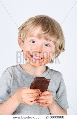 Young messy boy eating a chocolate bar with chocolate on his face