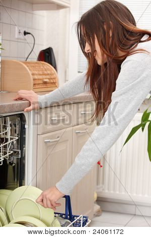 Giovane donna in cucina rassettando. Tirando fuori piatti dalla lavastoviglie