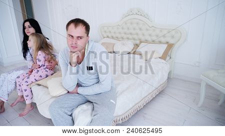 Upset Father Sitting Near Sad Wife With Little Daughter On Bed In Bedrom. Concept Of Family Quarrel.