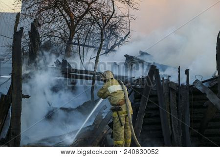 Firefighter Extinguishes The Fire. Fireman Holding A Hose With Water, Watering A Strong Stream Of Bu