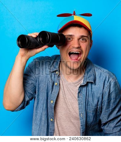 Young Nerd Man With Noob Hat Using A Binoculars On Blue Background