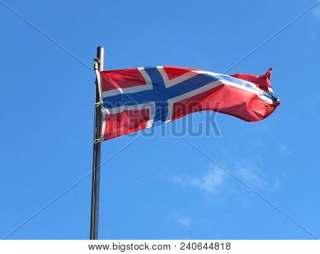 National Flag Of Norway On A Flagpole In Front Of Blue Sky.