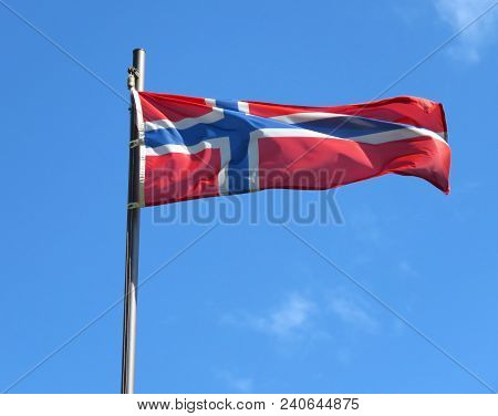 National Flag Of Norway On A Flagpole In Front Of Blue Sky.