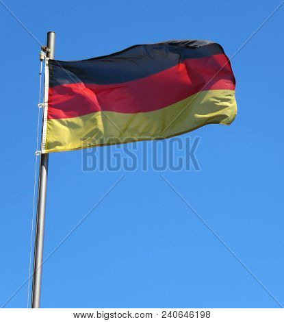 National Flag Of Germany On A Flagpole In Front Of Blue Sky.