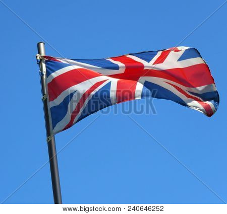 National Flag Of United Kingdom On A Flagpole In Front Of Blue Sky.