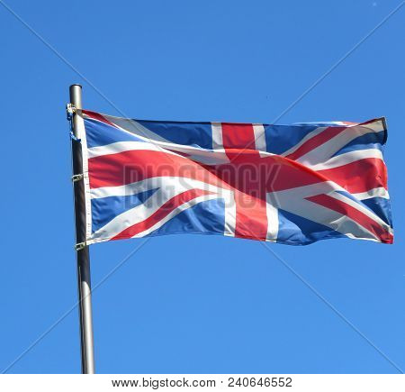 National Flag Of United Kingdom On A Flagpole In Front Of Blue Sky.