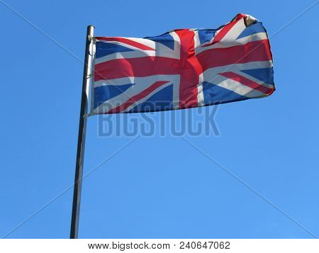 National Flag Of United Kingdom On A Flagpole In Front Of Blue Sky.