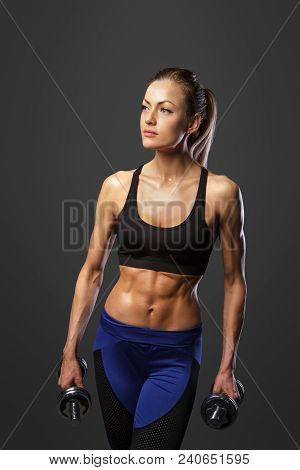 Sporty Woman Does The Exercises With Dumbbells On Dark Background. Photo Of Muscular Woman In Sports
