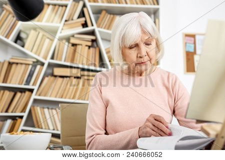 Reading Time. Concentrated Senior Woman Thumbing Through Book And Looking Down