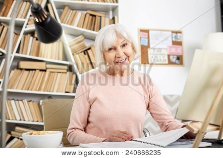 Home Assignment. Pleased Senior Woman Studying While Smiling To Camera