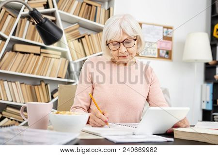 Educational Video. Focused Senior Woman Using Tablet While Writing Down