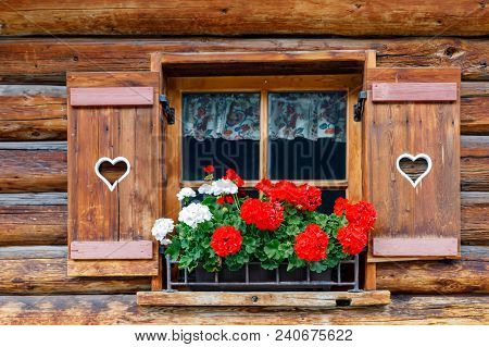 Typical Bavarian Or Austrian Wooden Window With Red Geranium Flowers On House In Austria Or Germany.