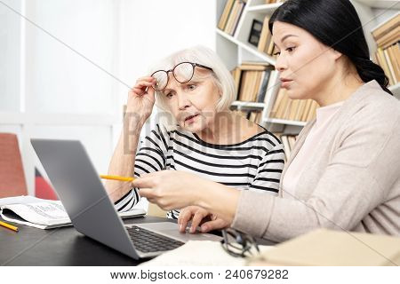 Look Here. Appealing Tutor And Senior Student Talking And Staring At Screen