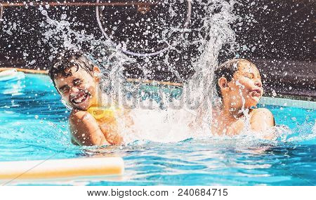 Two Boys At The Swimming Pool Splashing Water And Having Fun.