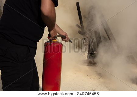 Young Man Pointing A Powder Type Fire Extinguisher Forwards Towards The Fire In A Serious Situation