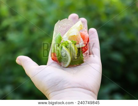 Melting Ice Cube With Strawberry, Lemon And Fresh Green Mint Leaves In A Hand