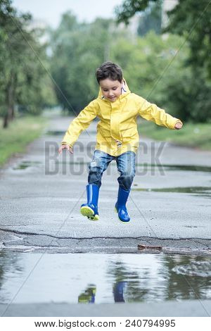 A Wet Child Is Jumping In A Puddle. Fun On The Street. Tempering In Summer