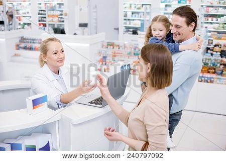 Let Me See. Satisfied Female Pharmacist Assisting Family And Posing In Drugstore