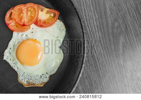 Fried Egg Fried With Chopped Tomatoes In A Cast-iron Frying Pan On A Wooden Table