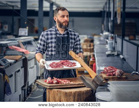 Bearded Butcher Dressed In A Fleece Shirt Serving Fresh Cut Meat In A Market.