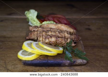 Breaded Chicken Meat With Salad And Lemon Resting On A Rustic Wooden Board