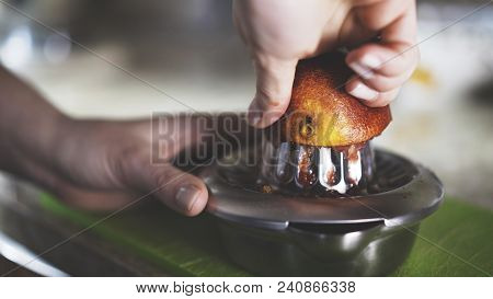 A Hand Squeezing Juice From An Orange On A Manual Glass Squeezer. Side View. Kitchen Background.