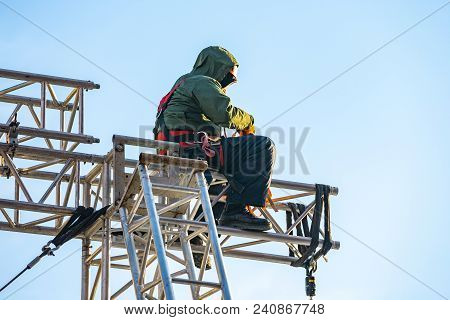 Industrial Climber In Uniform Sitting On A Building Structure. Alpinist Worker Checks His Equipment