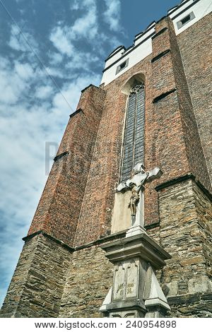 Cross And Facade Of A Medieval Defensive Church In The Gothic Style In Paczkow
