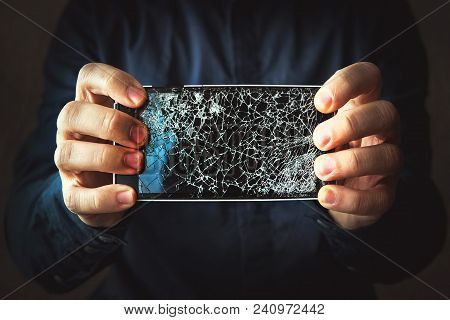 Broken Phone Screen In Hand In Dark Background. Guy Breaks A Black Modern Frameless Phone To Which T
