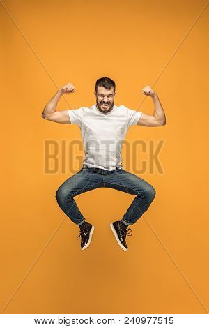 Freedom In Moving. Mid-air Shot Of Handsome Happy Young Man Jumping And Gesturing Against Orange Stu