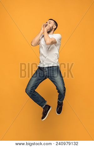Freedom In Moving. Mid-air Shot Of Handsome Happy Young Man Jumping And Gesturing Against Orange Stu