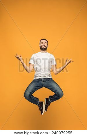 Freedom In Moving. Mid-air Shot Of Handsome Happy Young Man Jumping And Gesturing Against Orange Stu