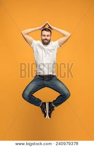 Freedom In Moving. Mid-air Shot Of Handsome Happy Young Man Jumping And Gesturing Against Orange Stu