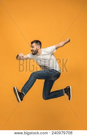Freedom In Moving. Mid-air Shot Of Handsome Happy Young Man Jumping And Gesturing Against Orange Stu