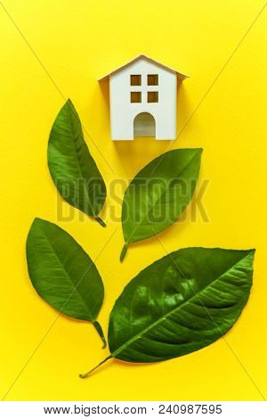 Miniature Toy Model House With Green Leaves On Yellow Colourful Trendy Backgdrop. Eco Village, Abstr
